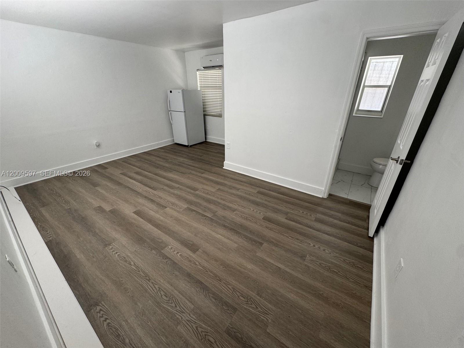 A room with wood-look flooring, a white refrigerator, and an adjacent bathroom with a toilet — 240 NW 64 str # 4, Miami FL 33150, MIAMI, FL