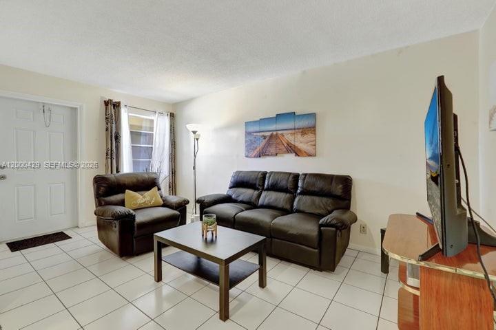 A living room features white tile floors, a black leather sofa and armchair, and a television — 2145 Pierce St # 326, Hollywood FL 33020, HOLLYWOOD, FL