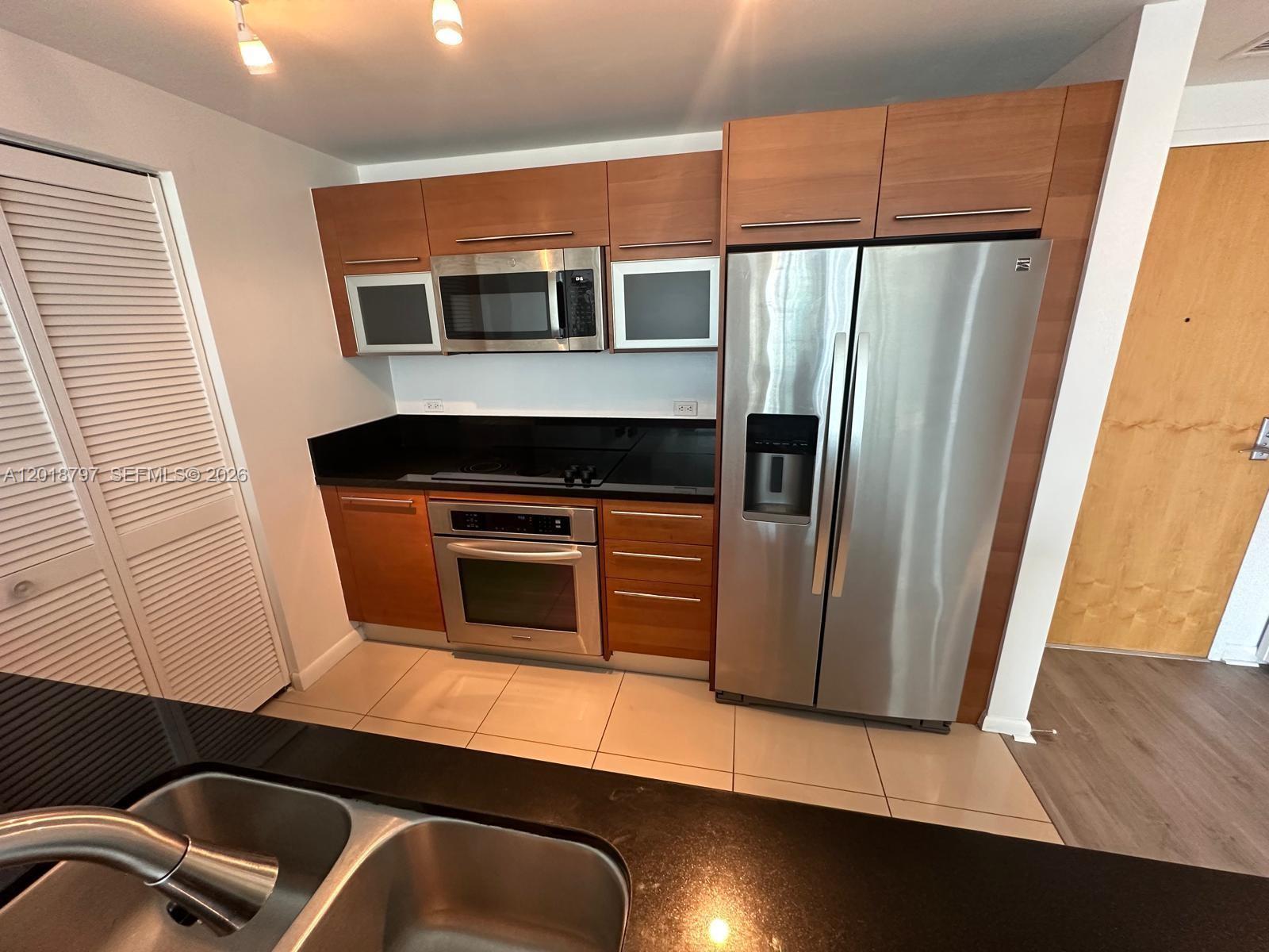 A kitchen features wood cabinets, stainless steel appliances, and black countertops — 244 Biscayne Blvd # 1910, Miami FL 33132, MIAMI, FL
