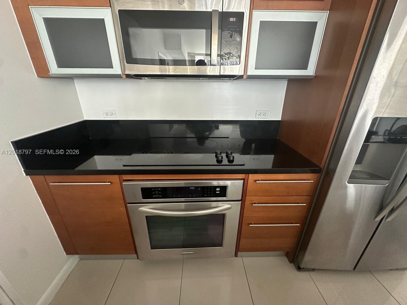 A kitchen features wood cabinets, stainless steel appliances, and a black countertop — 244 Biscayne Blvd # 1910, Miami FL 33132, MIAMI, FL