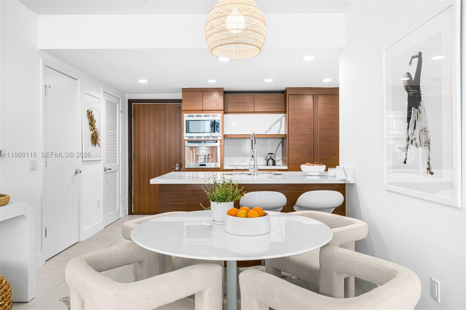 A modern kitchen features wood cabinetry, a marble-topped island, and a round dining table — 5875 Collins Ave # 906, Miami Beach FL 33140, MIAMI BEACH, FL