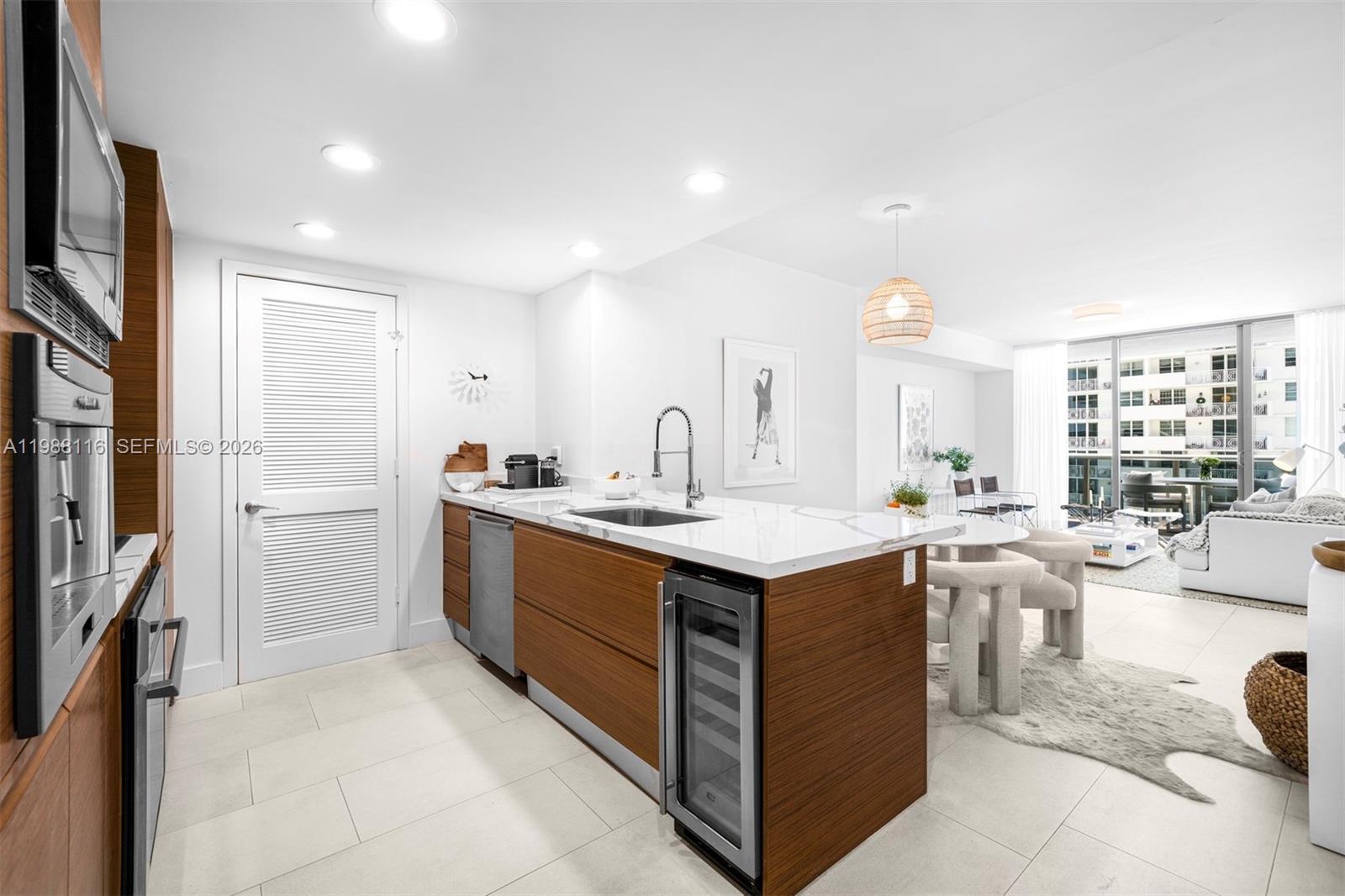 A modern kitchen features wood cabinetry, a white stone island, and an open living area — 5875 Collins Ave # 906, Miami Beach FL 33140, MIAMI BEACH, FL