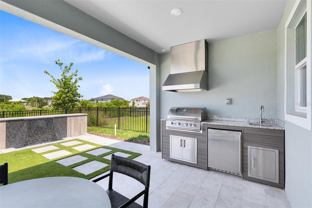 A covered outdoor kitchen features a stainless steel grill, hood, sink, and stone patio flooring — 403 WINTER GROVE BOULEVARD, WINTER GARDEN, FL