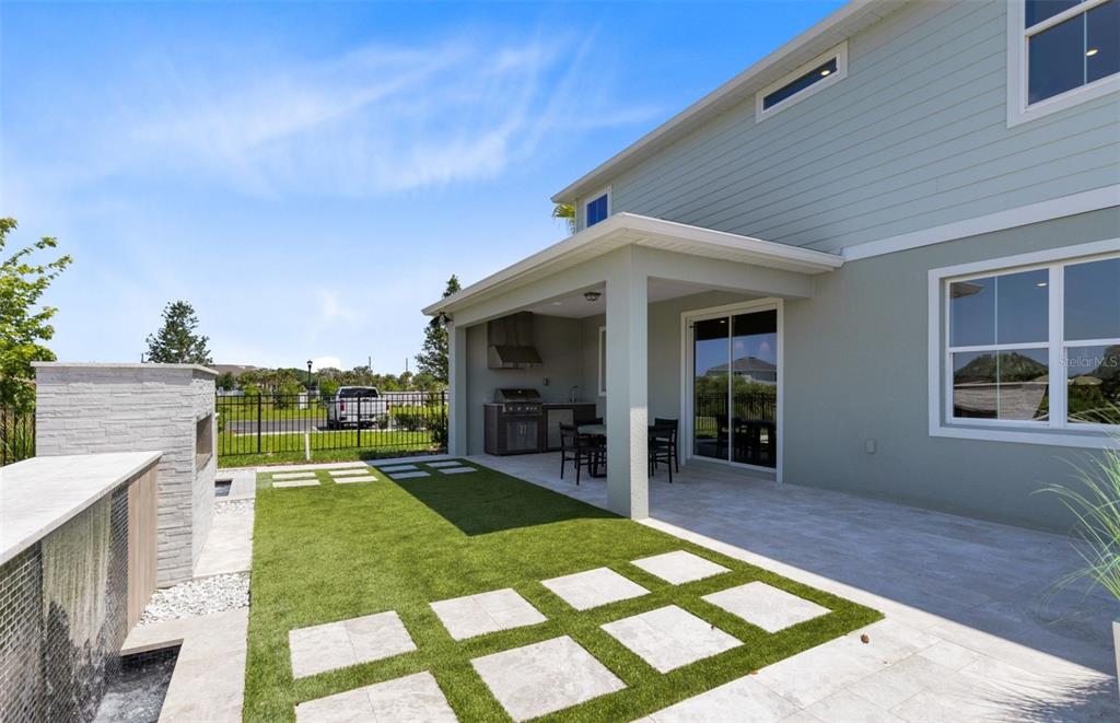 A backyard patio features a covered outdoor kitchen, artificial turf, and a stone fireplace — 403 WINTER GROVE BOULEVARD, WINTER GARDEN, FL