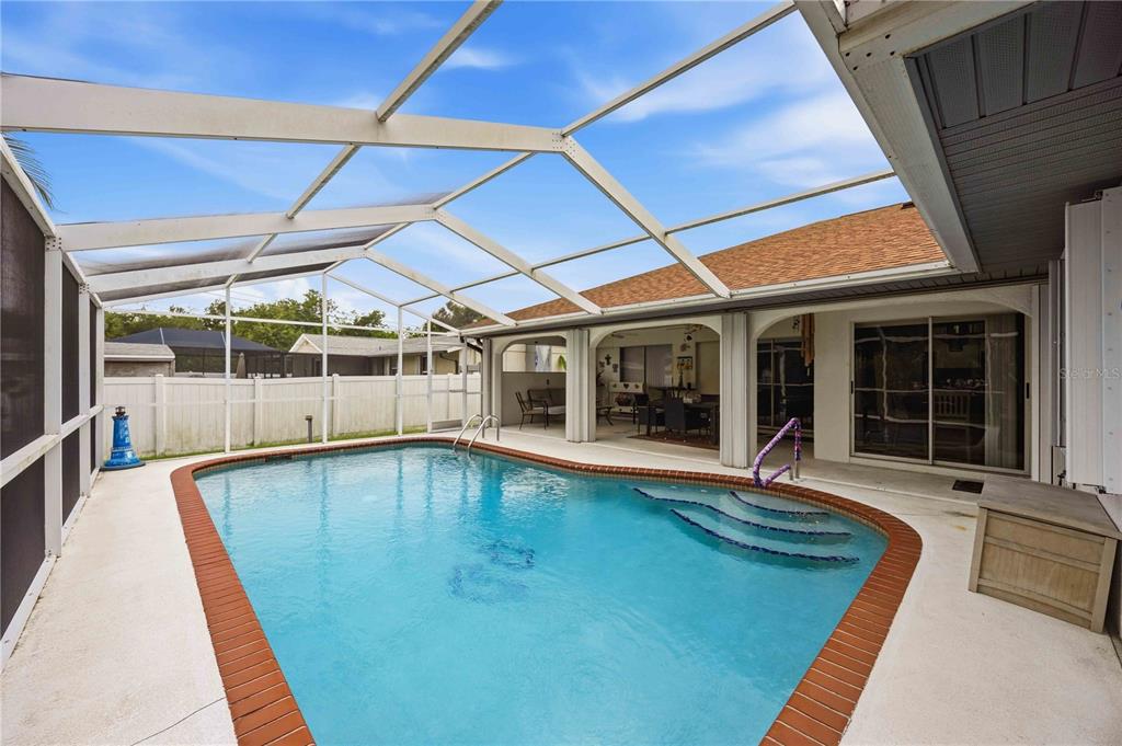 A screened-in swimming pool with a brick border sits on a patio next to a house — 273 CICERO STREET NW, PORT CHARLOTTE, FL