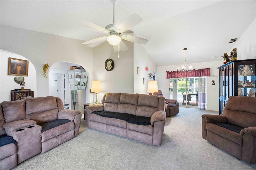 A living room features brown reclining furniture, beige carpeting, a ceiling fan, and arched doorways — 273 CICERO STREET NW, PORT CHARLOTTE, FL
