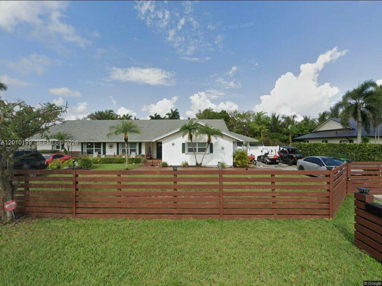 A single-story white house with a brown wooden fence stands behind a green lawn — 29490 SW 193 AVE, Homestead FL 33030, HOMESTEAD, FL