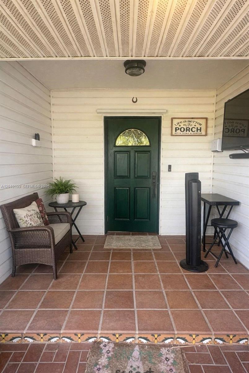 A covered porch features a dark green front door, tiled flooring, and outdoor furniture — 29490 SW 193 AVE, Homestead FL 33030, HOMESTEAD, FL