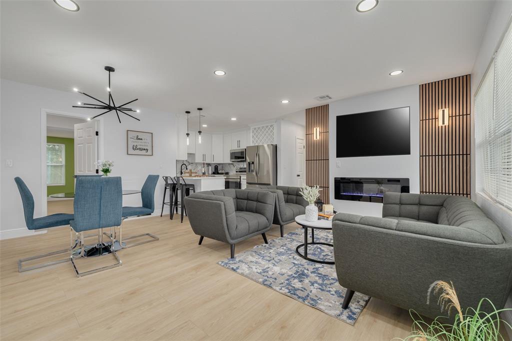 An open-concept living and dining area features light wood floors, gray furniture, and a fireplace — 11189 108TH WAY, LARGO, FL