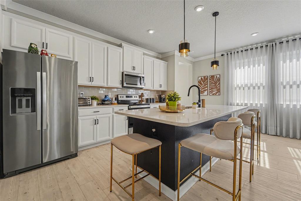 A kitchen features white cabinets, a dark island with bar stools, and stainless steel appliances — 5975 TIMBERDALE AVENUE, WESLEY CHAPEL, FL