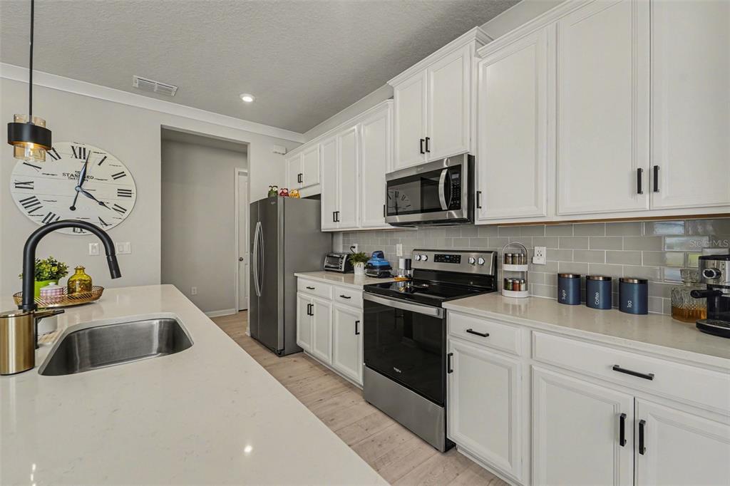 A modern kitchen features white cabinets, stainless steel appliances, quartz countertops, and a subway tile backsplash — 5975 TIMBERDALE AVENUE, WESLEY CHAPEL, FL