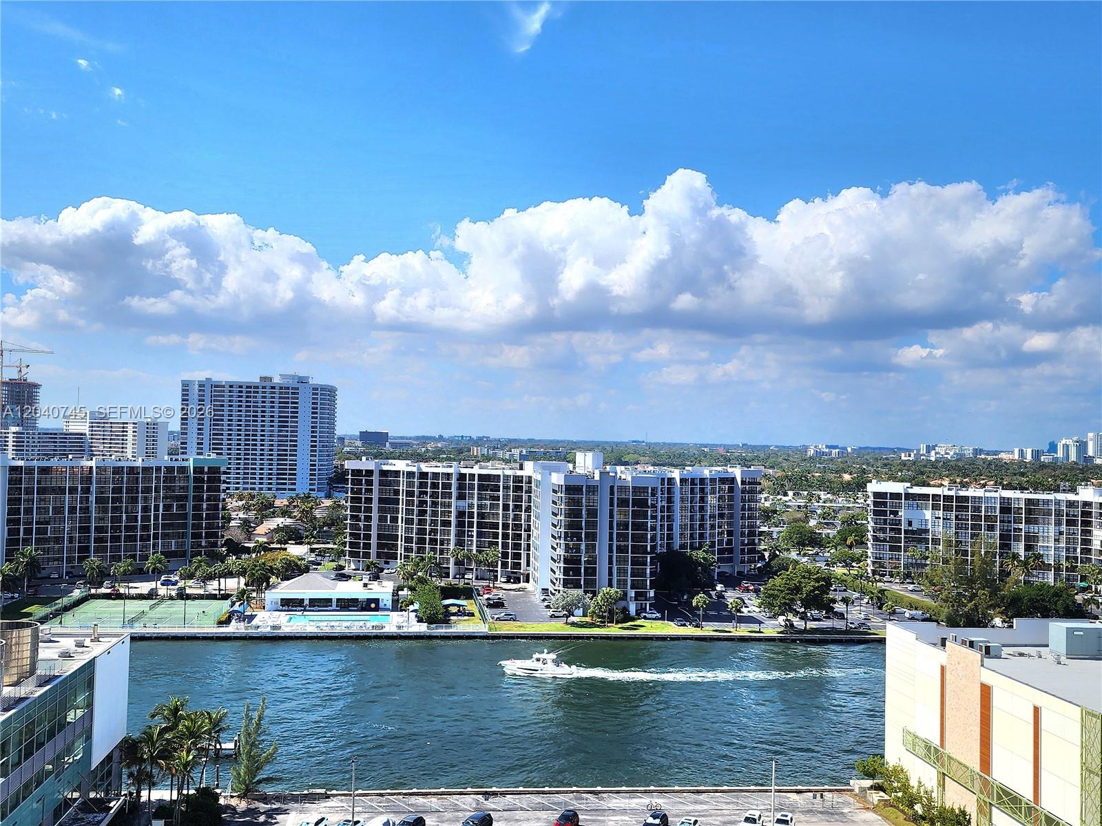 An elevated view shows a waterway with a boat passing apartment buildings and tennis courts — 3505 S Ocean Dr # 1502, Hollywood FL 33019, HOLLYWOOD, FL
