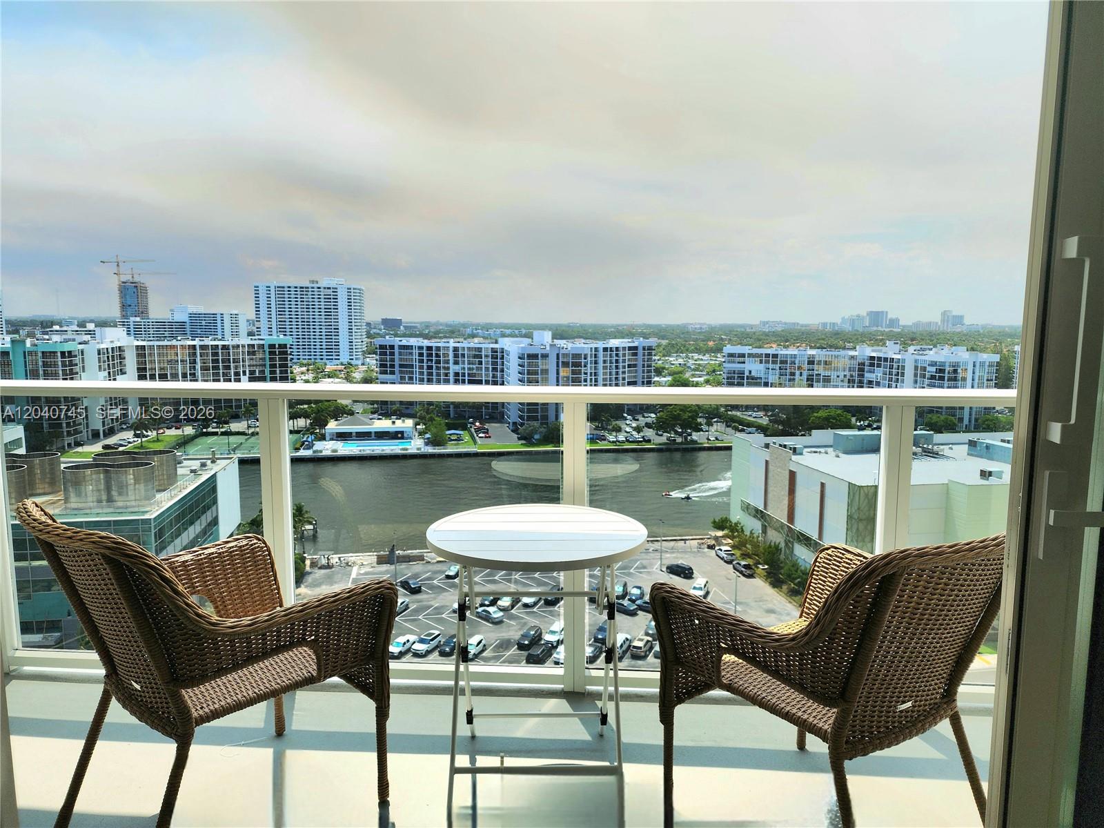 A balcony features two wicker chairs and a small table overlooking a waterway and city — 3505 S Ocean Dr # 1502, Hollywood FL 33019, HOLLYWOOD, FL