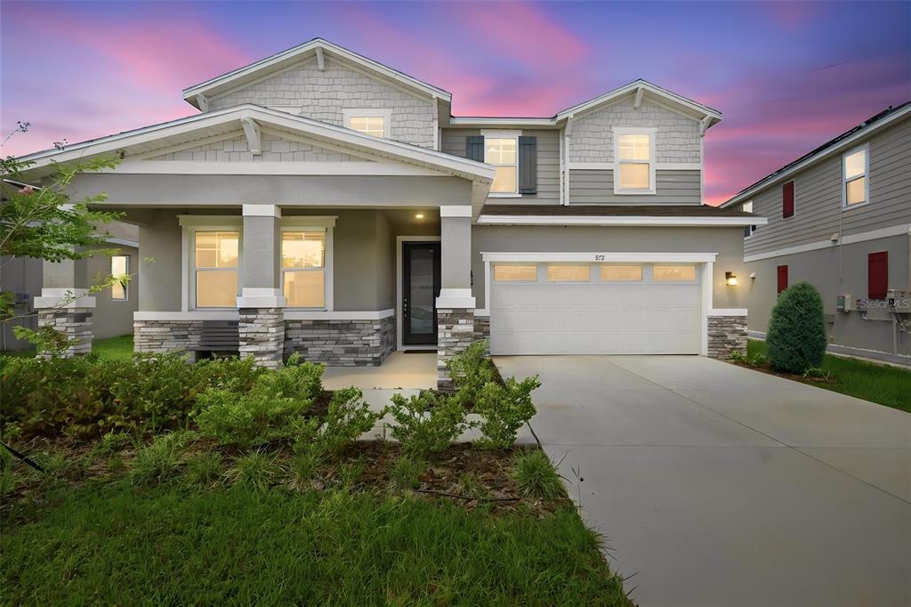 A two-story suburban house features a covered front porch, stone accents, and a two-car garage — 832 GRIFFON AVENUE, LAKE ALFRED, FL