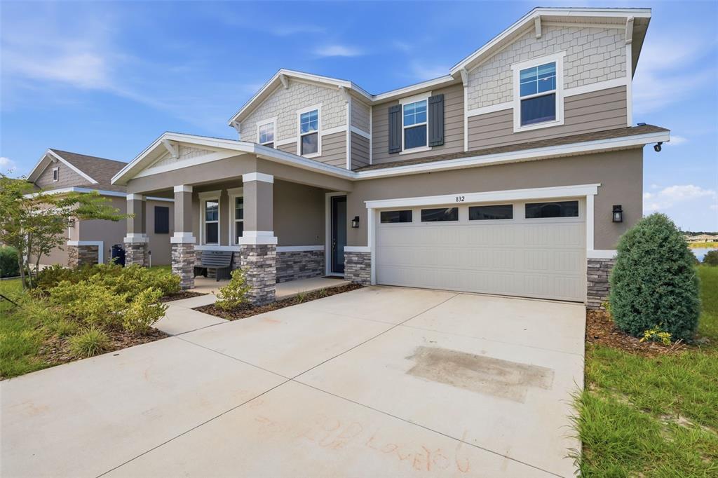 A two-story suburban house features a stone-accented porch, a two-car garage, and tan siding — 832 GRIFFON AVENUE, LAKE ALFRED, FL