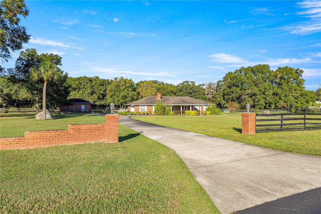 A long concrete driveway leads to a single-story brick house on a large grassy lot — 9812 SW 74TH AVENUE, OCALA, FL