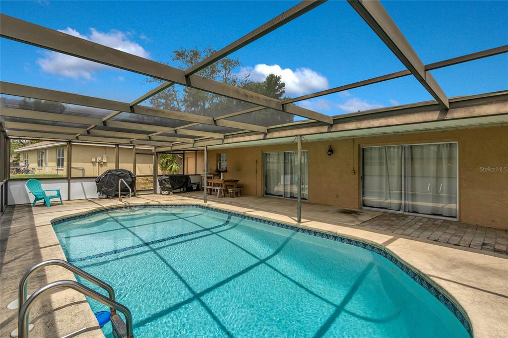 A screened-in patio features a swimming pool, a concrete deck, and sliding glass doors — 5262 WOODRIDGE LANE, SPRING HILL, FL