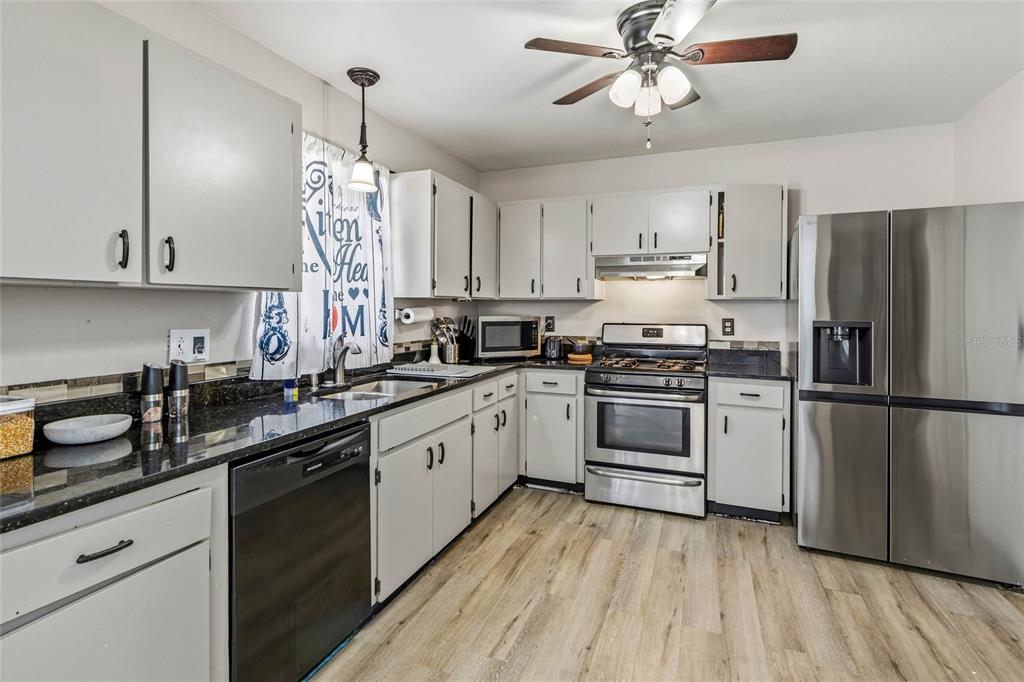 A kitchen features white cabinets, black countertops, stainless steel appliances, and light wood-look flooring — 5262 WOODRIDGE LANE, SPRING HILL, FL