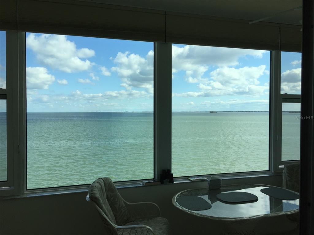 A sunroom features large windows overlooking a wide expanse of water under a blue sky — 7 DUNOON PLACE UNIT 303, DUNEDIN, FL