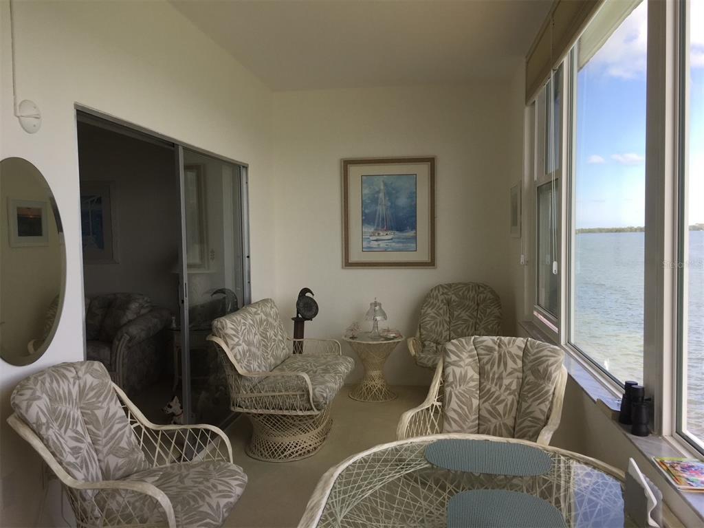 A sunroom features wicker furniture, a glass-topped table, and large windows overlooking a body of water — 7 DUNOON PLACE UNIT 303, DUNEDIN, FL