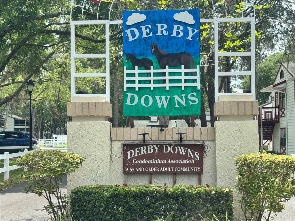 A sign for Derby Downs, a 55 and older condominium community, stands outdoors near trees — 7817 MIDWAY DRIVE TERRACE UNIT A 103, OCALA, FL