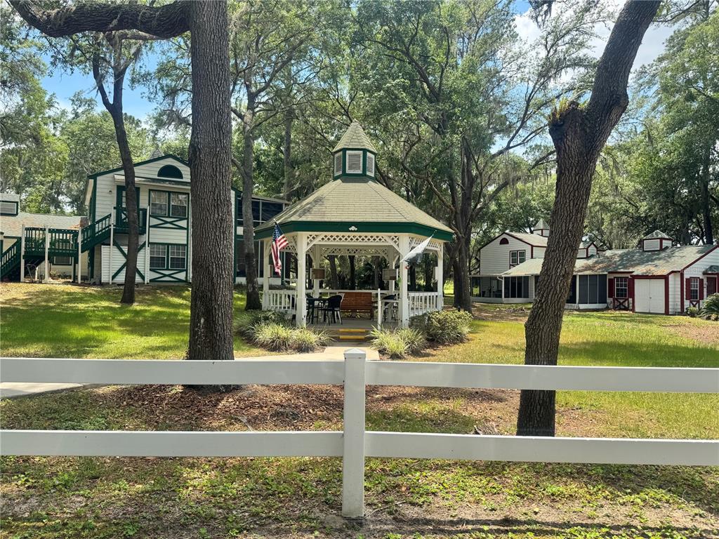 A white gazebo stands in a grassy yard surrounded by trees and several white buildings — 7817 MIDWAY DRIVE TERRACE UNIT A 103, OCALA, FL