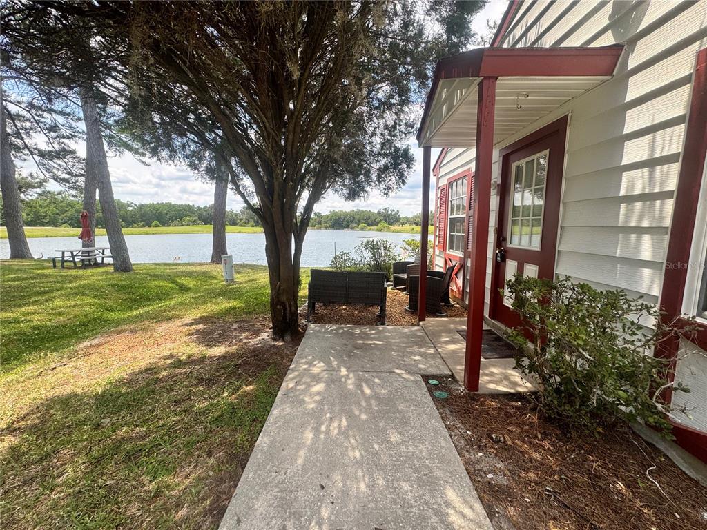 A concrete walkway leads to a house entrance with a red door overlooking a lake — 7817 MIDWAY DRIVE TERRACE UNIT A 103, OCALA, FL