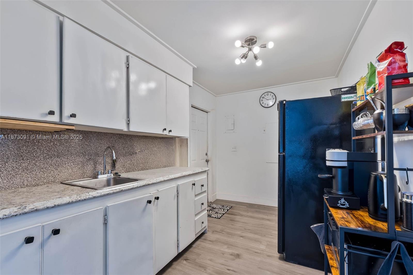 A kitchen features white cabinets, a granite countertop, a stainless steel sink, and a refrigerator — 180 NW 59th St, Miami FL 33127, MIAMI, FL