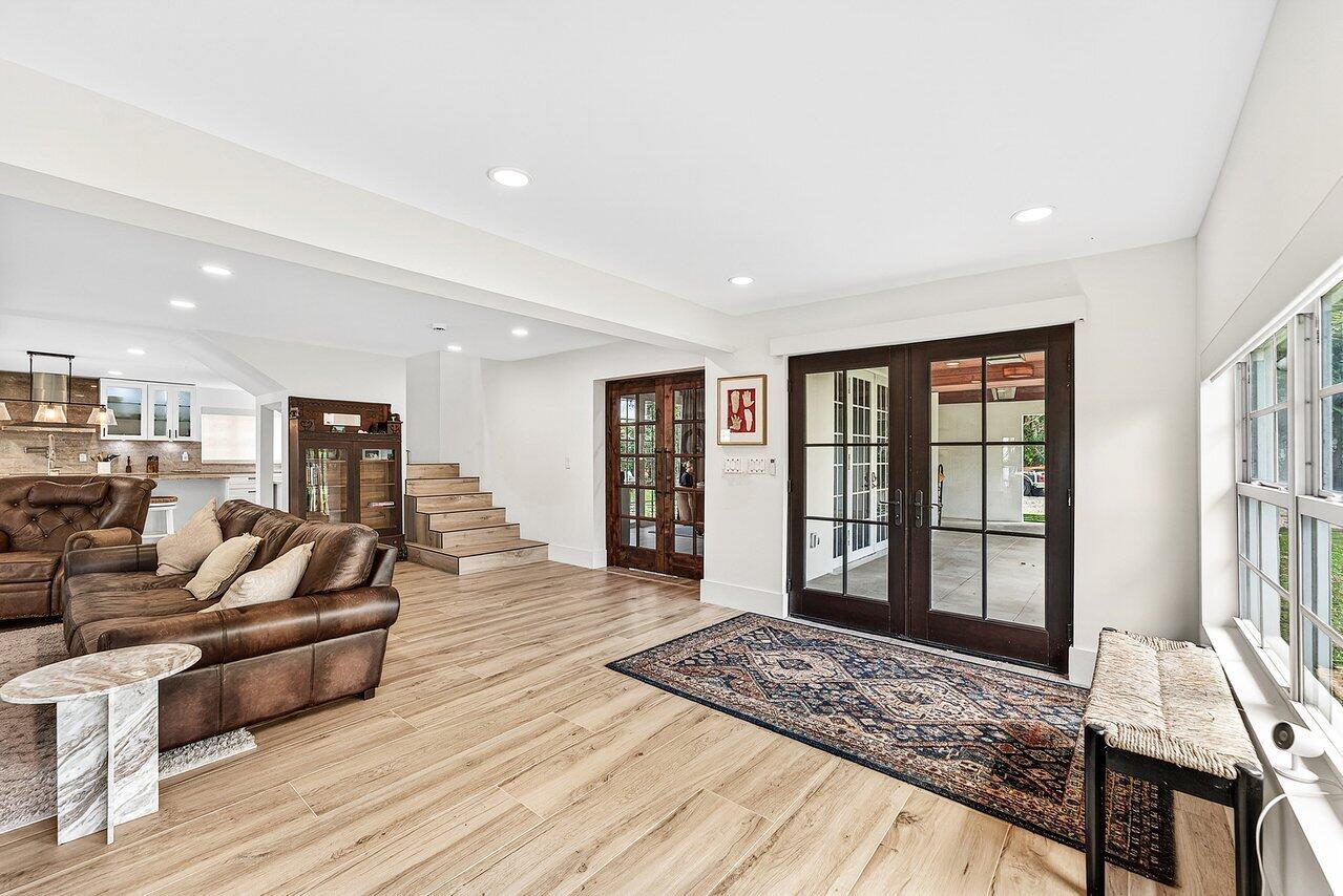 A living room with wood-look flooring, a leather sofa, stairs, and glass doors to a patio — 321 SW 1st Avenue, Boynton Beach FL 33435, BOYNTON BEACH, FL