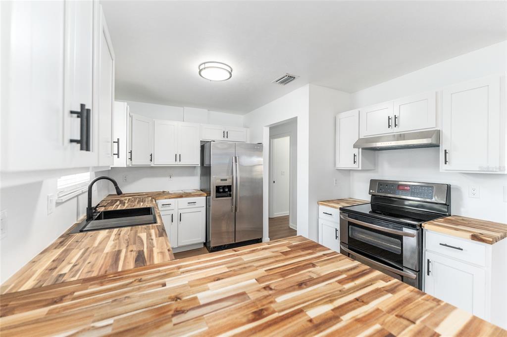 A kitchen features white cabinets, stainless steel appliances, and wood butcher block countertops — 5701 SW 47TH PLACE, GAINESVILLE, FL