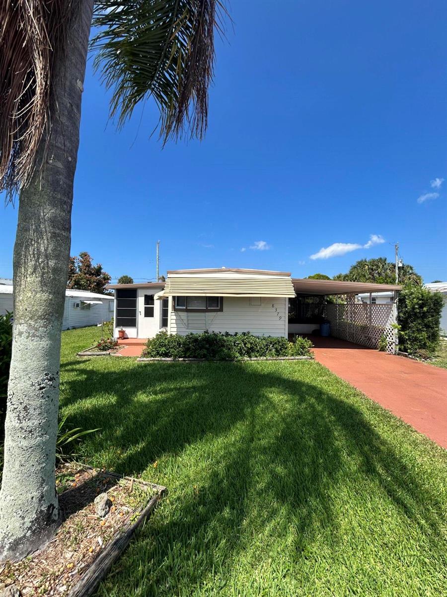 A single-story mobile home with a carport, white siding, and a front lawn — 8379 SE Eagle Avenue, Hobe Sound FL 33455, HOBE SOUND, FL
