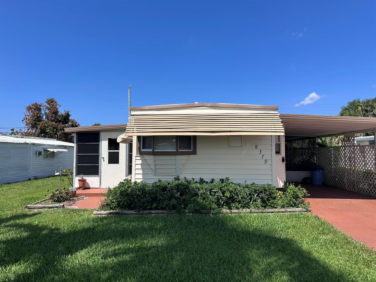 A single-story mobile home with a front awning, carport, and a small landscaped garden — 8379 SE Eagle Avenue, Hobe Sound FL 33455, HOBE SOUND, FL