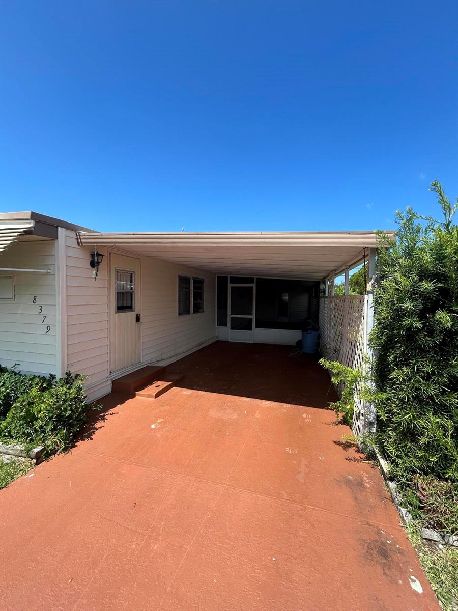 A beige manufactured home features a covered carport and a screened-in porch entrance — 8379 SE Eagle Avenue, Hobe Sound FL 33455, HOBE SOUND, FL