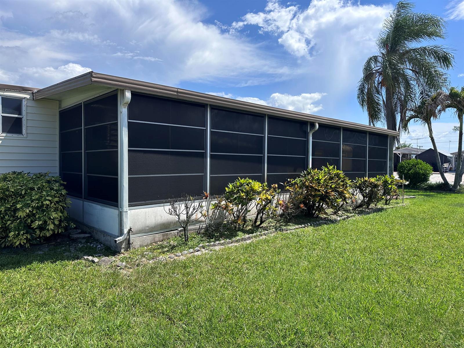 A mobile home features a large screened-in porch with a metal roof and landscaping — 8379 SE Eagle Avenue, Hobe Sound FL 33455, HOBE SOUND, FL