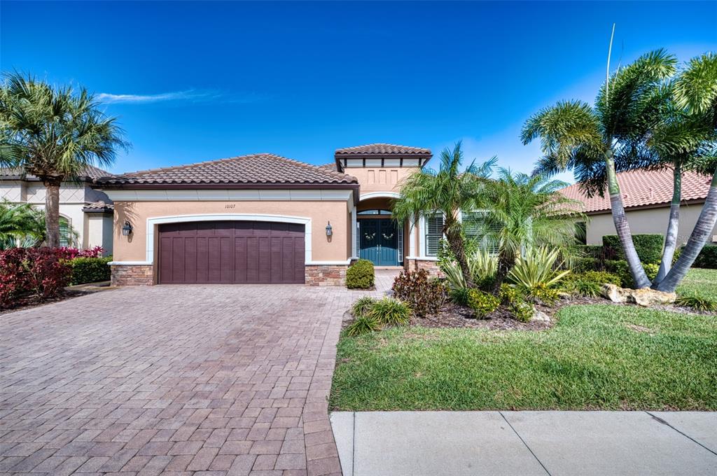 A single-story house with a brown garage door, tiled roof, and palm trees in front — 10107 WICKER PARK PLACE, PALMETTO, FL