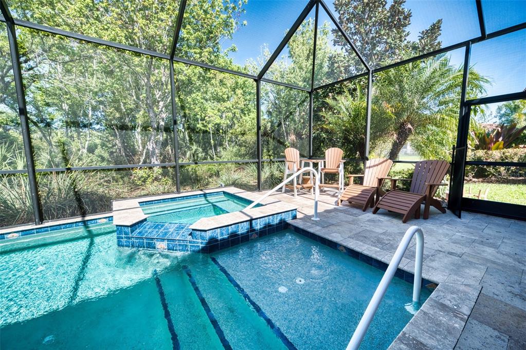 A screened-in pool area features a raised tiled spa, lounge chairs, and stone decking — 10107 WICKER PARK PLACE, PALMETTO, FL