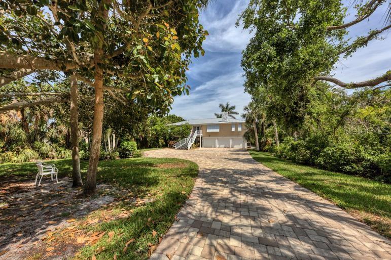 A paved driveway leads to a raised house with a three-car garage and lush landscaping — 7505 MANASOTA KEY RD, ENGLEWOOD, FL