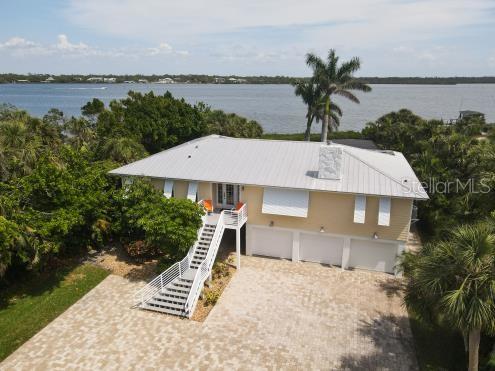 A yellow elevated house with a metal roof, three garage doors, and a front staircase — 7505 MANASOTA KEY RD, ENGLEWOOD, FL