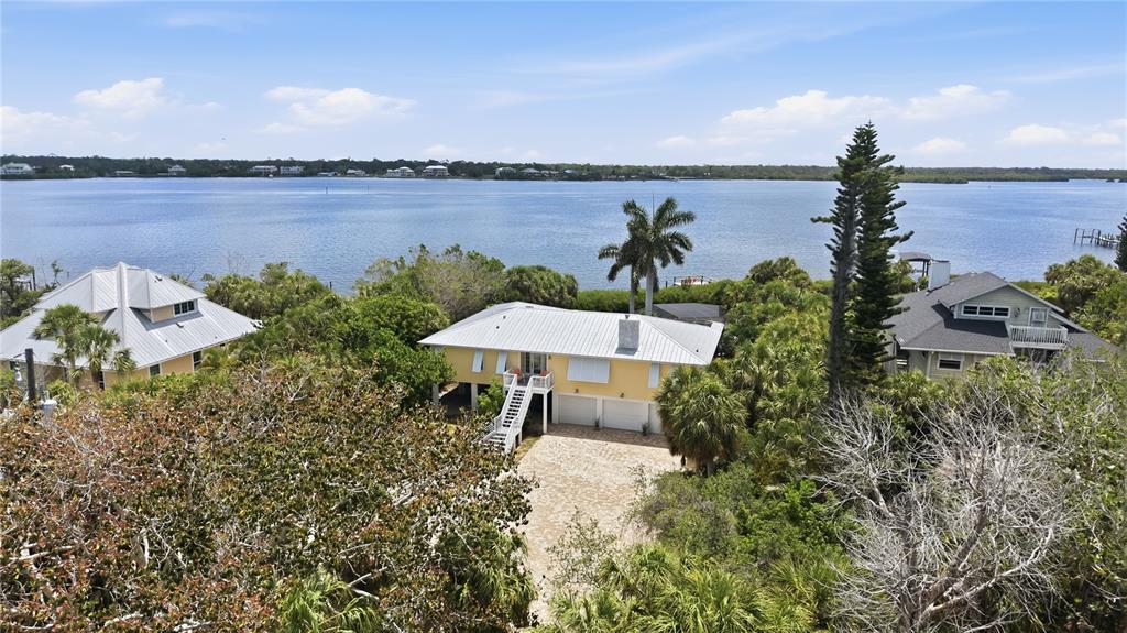 An elevated yellow house with a metal roof sits near a large body of water — 7505 MANASOTA KEY RD, ENGLEWOOD, FL