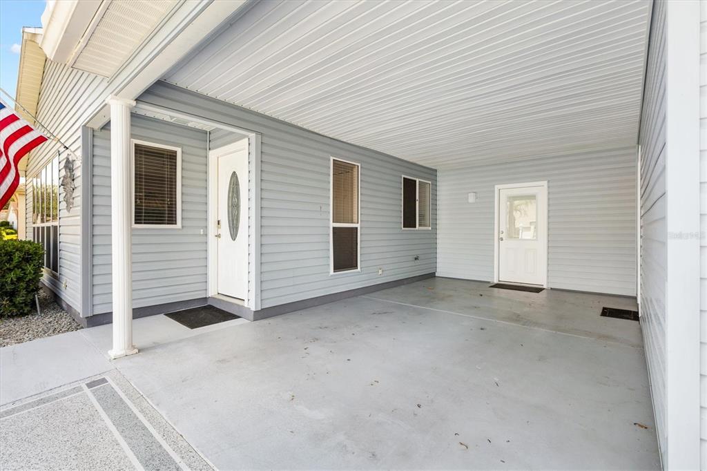 A covered concrete carport features light blue siding, two white doors, and several windows — 406 DEL MAR DRIVE, LADY LAKE, FL
