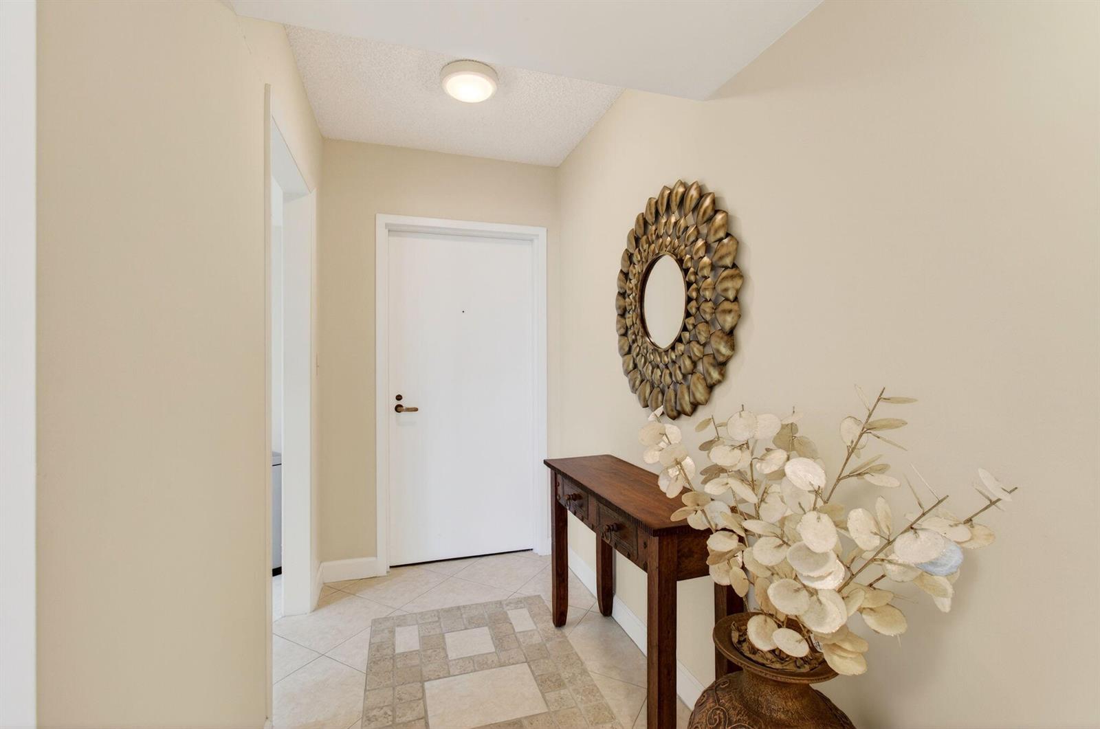 A foyer features a white door, a wooden console table, a decorative mirror, and tile flooring — 4740 S Ocean Boulevard # 702, Highland Beach FL 33487, HIGHLAND BEACH, FL