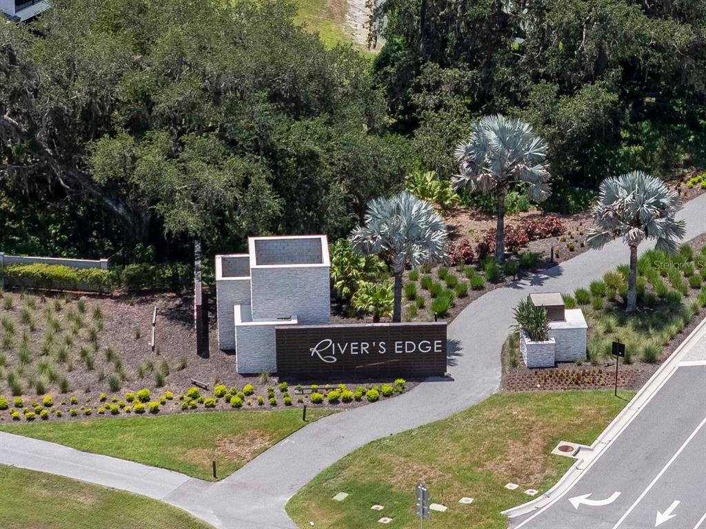 An aerial view shows the River's Edge community entrance sign surrounded by landscaping and palm trees — 2639 YACHT PLACE, WESLEY CHAPEL, FL