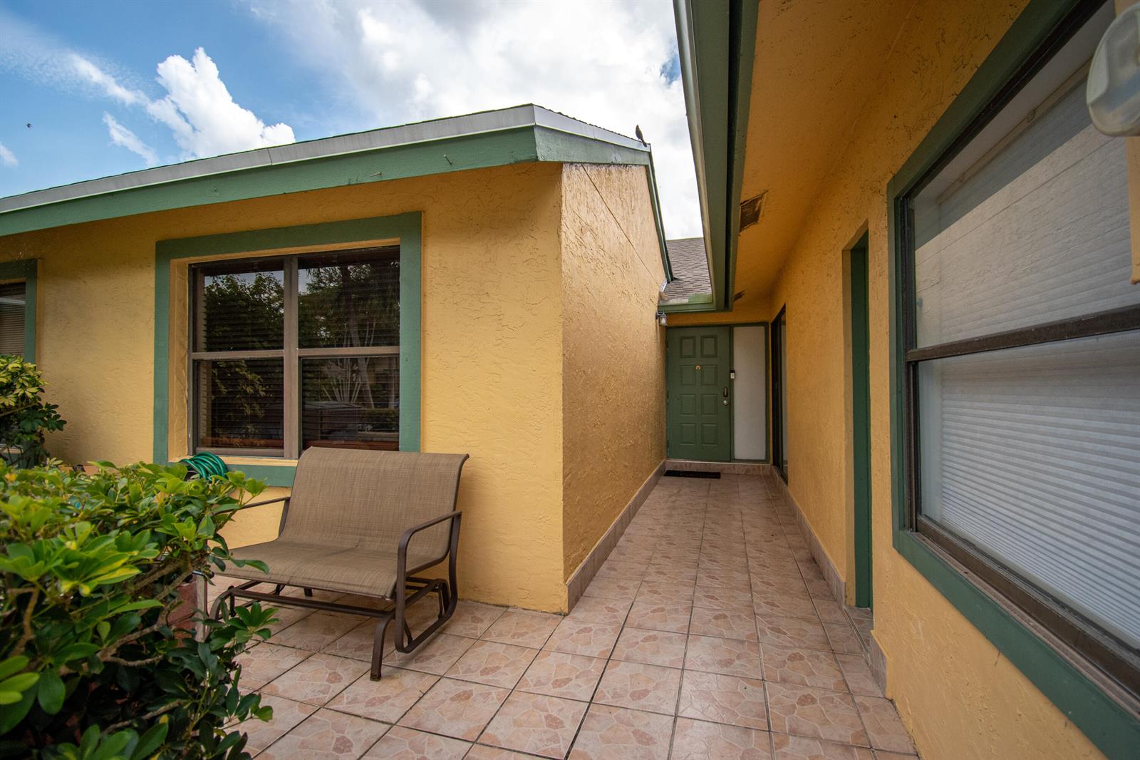 A tiled patio leads to a green front door between two yellow exterior walls — 7964 Little Lane, Boca Raton FL 33433, BOCA RATON, FL