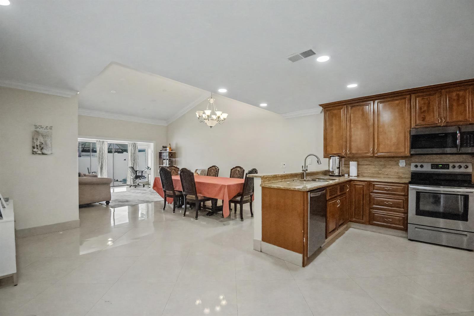 An open-concept kitchen and dining area features wood cabinets, granite countertops, and tile flooring — 7964 Little Lane, Boca Raton FL 33433, BOCA RATON, FL