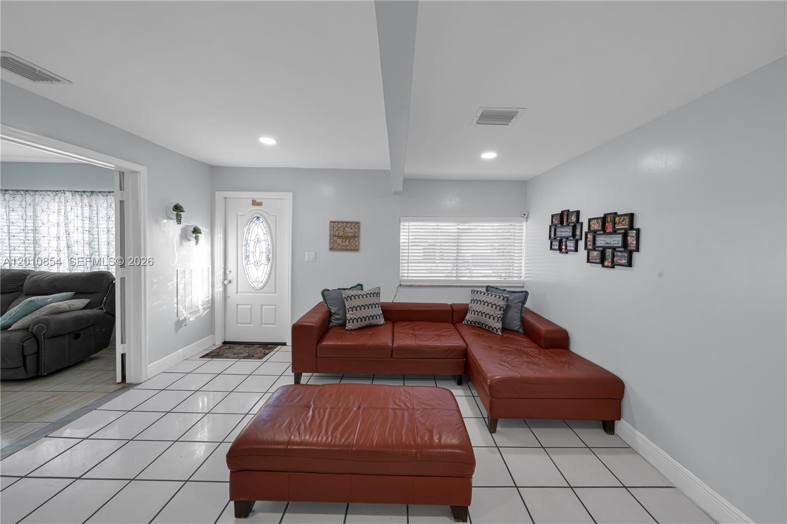 A living room features a red leather sectional, matching ottoman, and white tile flooring — 11021 SW 4th St, Sweetwater FL 33174, SWEETWATER, FL