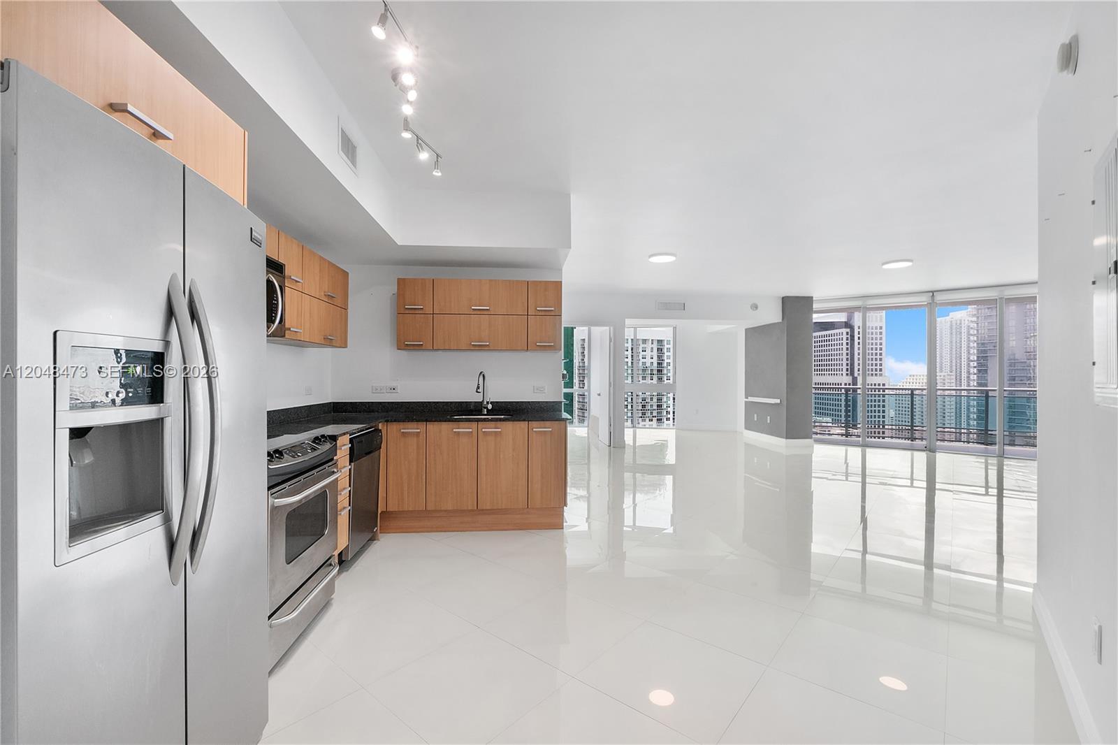 A modern kitchen with light wood cabinets and stainless steel appliances opens to a living area — 350 S Miami Ave # 3702, Miami FL 33130, MIAMI, FL