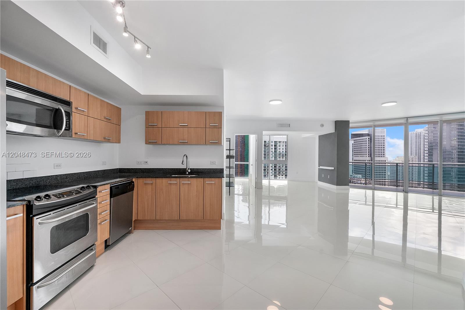 A modern kitchen with wood cabinets and stainless steel appliances opens to a bright living area — 350 S Miami Ave # 3702, Miami FL 33130, MIAMI, FL