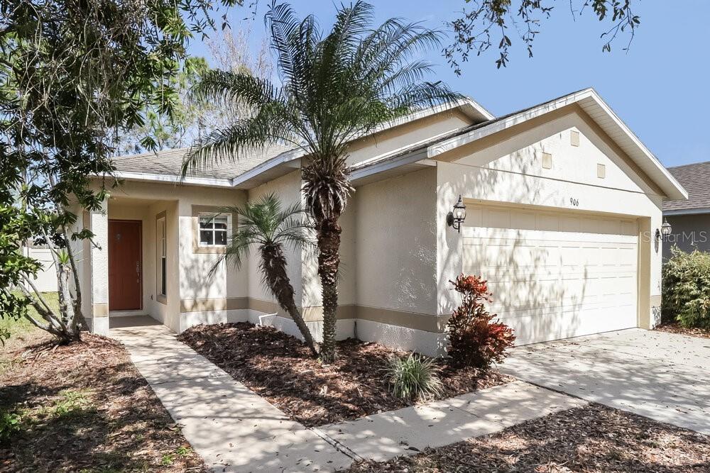 A single-story house with a beige stucco exterior, a two-car garage, and a palm tree — 906 LARWOOD PINE DRIVE, RUSKIN, FL