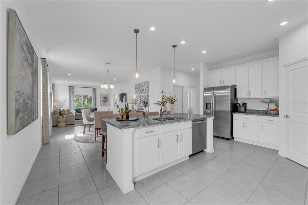 A kitchen with white cabinets and a granite island overlooks an open-concept living area — 10123 MORNING MEADOWLARK TRAIL, PARRISH, FL