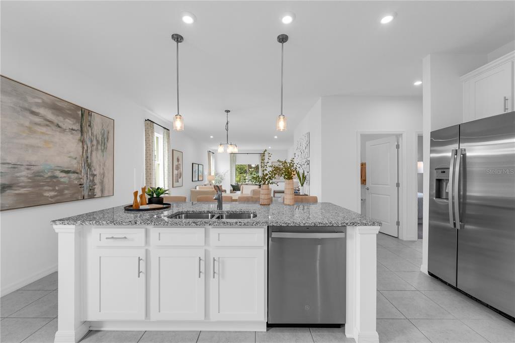 A kitchen island with a granite countertop and stainless steel dishwasher faces an open living area — 10123 MORNING MEADOWLARK TRAIL, PARRISH, FL
